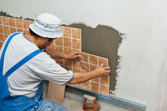 Ididikit ng master ang mga tile sa dingding